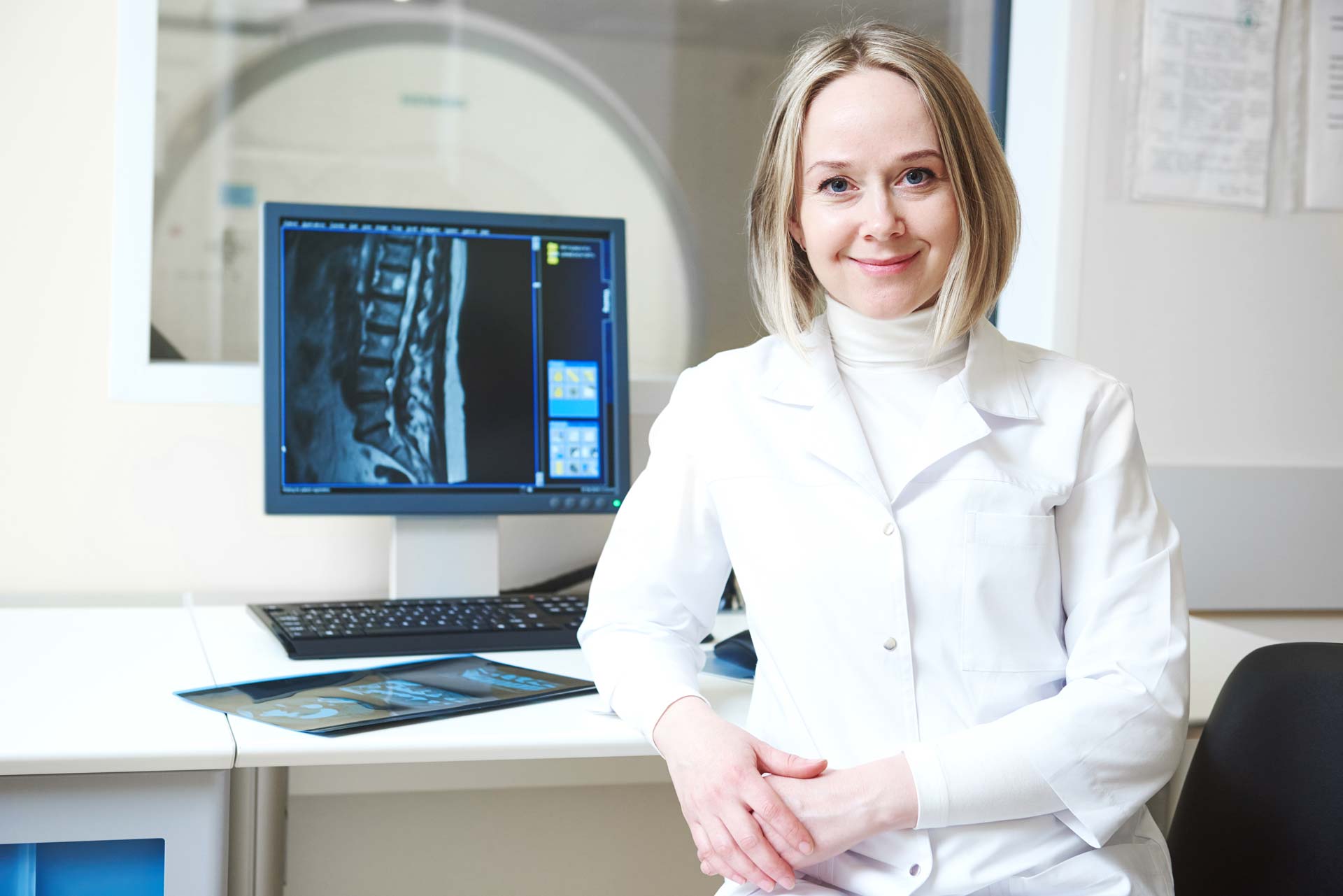 MRI Technologist sitting at desk with the MRI room in the background